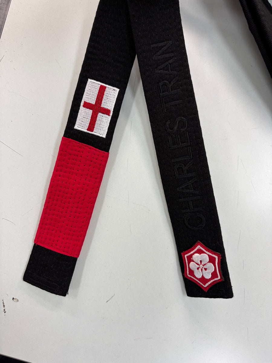 Black belt with an England flag above the red rank bar on one end and tone-on-tone name embroidery above the KANJI logo on the other