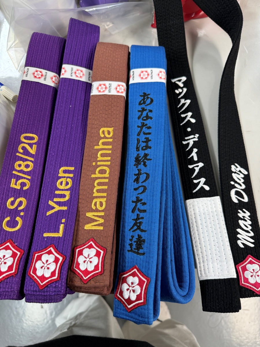 Purple, brown, blue and black customer belts with embroidered names, a date and Japanese text